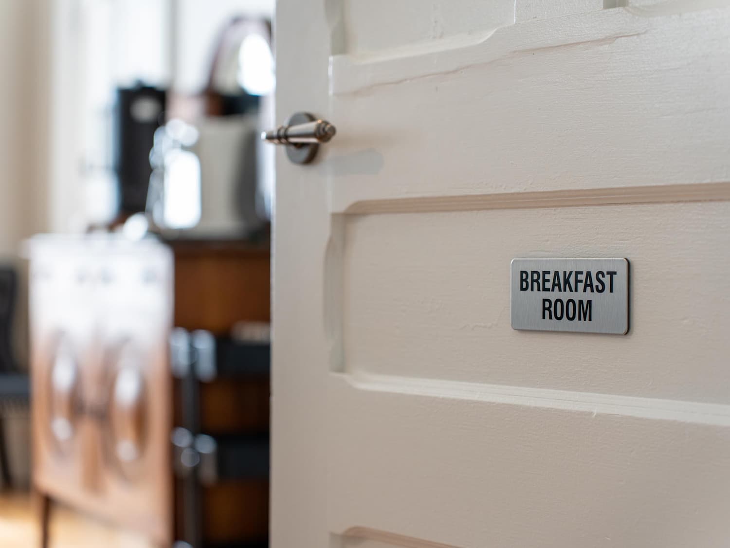 A white door with a sign reading Breakfast Room is partially open, revealing a glimpse of a furnished room beyond.